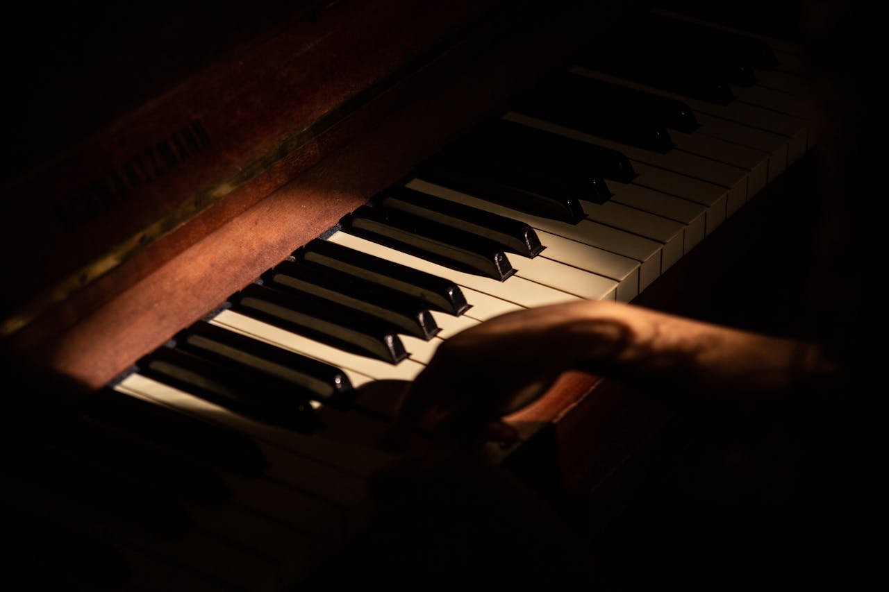 A tranquil scene of a pianist's hand gently playing a piano in dim lighting.